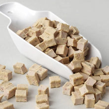 Cubes of tofu on a white dish and scattered on a light gray surface
