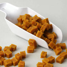White scoop filled with orange square-shaped treats on a light gray background
