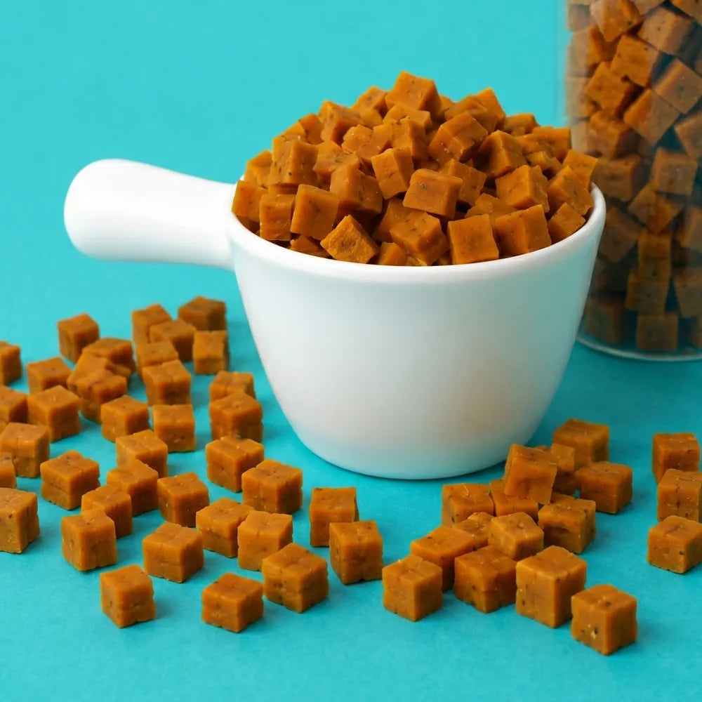 Brown square-shaped treats in a white bowl on a blue background