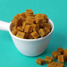 White bowl filled with square-shaped yellow dog treats on a teal background