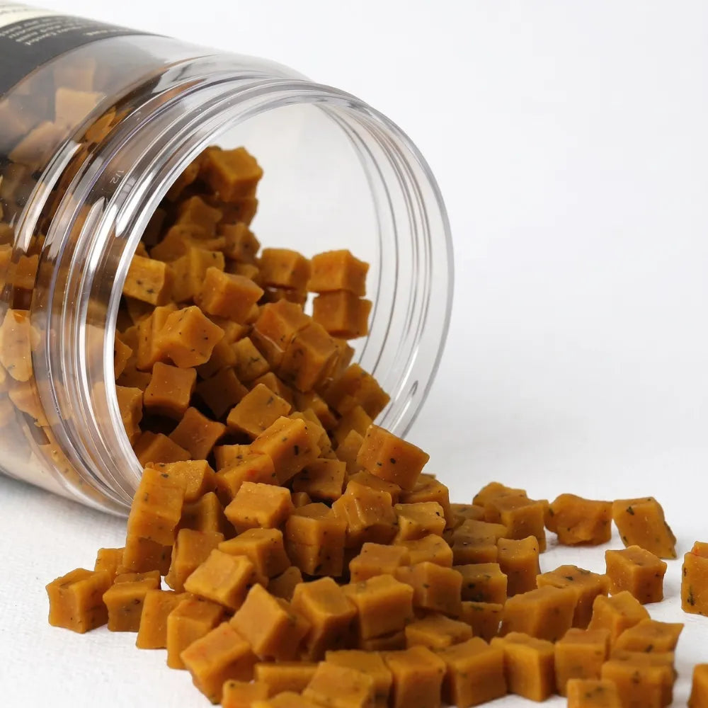 Clear jar filled with square-shaped brown dog treats on a white background